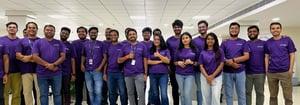 Group of Nextuple employees wearing matching purple Nextuple shirts pose together at a hackathon.