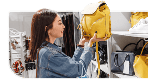 A shopper holds up a yellow handbag at a fashion store.