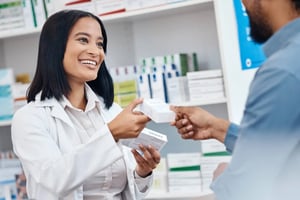 A smiling pharmacist hands a customer their medication. 