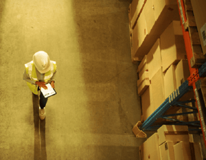 An inventory planner checks inventory levels on a tablet walking through a warehouse. 