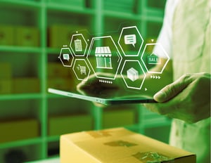 Ecommerce and retail merchant holding a tablet with superimposed icons of boxes, storefronts, warehouses, and shopping carts—representing connected, end-to-end inventory planning across the supply chain.