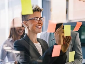 A group of three business people smile while writing on yellow and orange sticky notes during a Strategy and Consulting session.