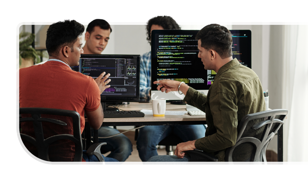 a group of four developers huddle around computers. a group of four developers huddle around computers.